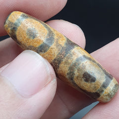"Image of an antique agate bead from Tibet, Himalayan region, featuring a Dzi pendant with 3 eyes, symbolizing spiritual protection and good fortune, showcasing a rare and unique cultural artifact."